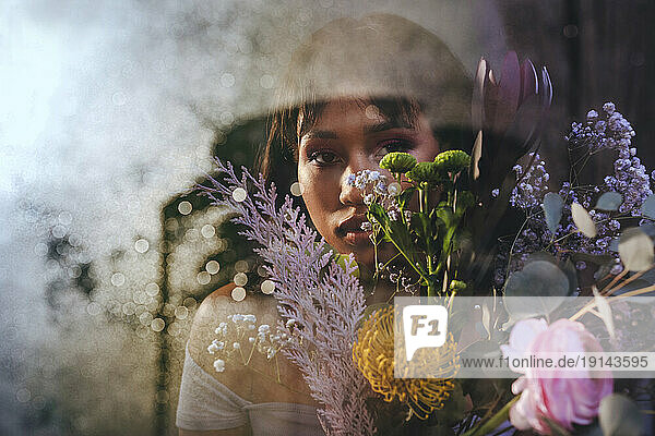 Woman with bouquet of flowers behind glass wall