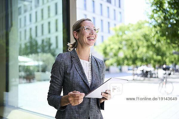 Happy businesswoman holding tablet PC near building