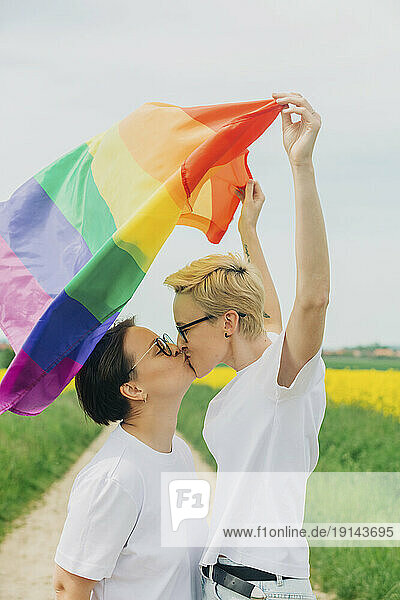 Loving lesbians with rainbow flag kissing each other at field