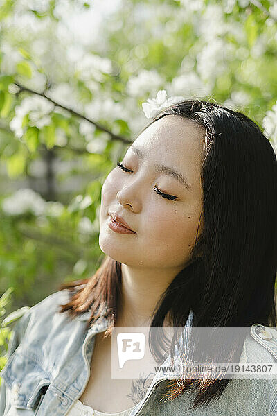 Young woman with eyes closed by flowering tree