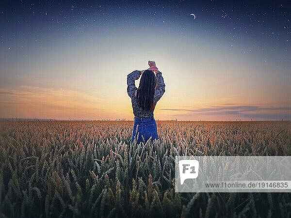 Mädchen im goldenen Weizenfeld bei Sonnenuntergang. Schöne Dämmerungslandschaft unter dem sommerlichen Sternenhimmel mit Mondsichel. Magische natürliche Szene  Freiheit Konzept