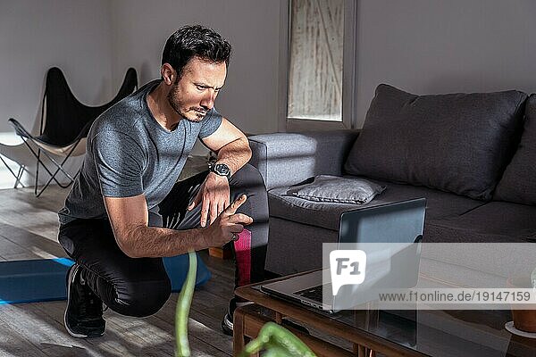 Latino Fitnesstrainer  der vor seinem Laptop online unterrichtet. Arbeit zu Hause  Online Training mit Kunden
