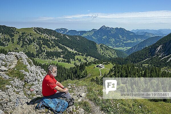 Wanderer  Senior  65  hält Gipfelrast auf dem Taubenstein und genießt die Aussicht auf das Taubensteinhaus  Breitenstein und Wendelstein  Spitzingsee  Mangfallgebirge  Oberbayern  Bayern  Deutschland  Europa