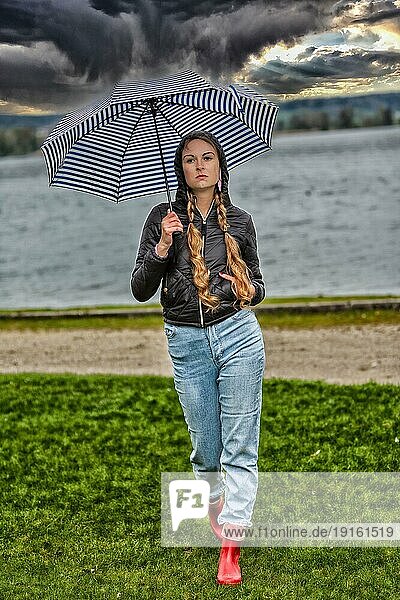 Junge Frau mit Zöpfen und Regenschirm am See  dramatische Wolken