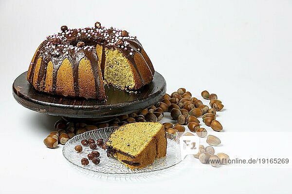 Veganer Haselnusskuchen auf Servierteller aus Holz  angeschnitten  Kuchenstück auf Glasteller  Haselnüsse daneben  weißer Hintergrund  Kopierraum