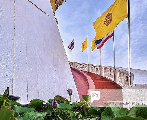 Reihe von thailändischen nationalen  buddhistischen und königlichen Fahnen entlang einer Wendeltreppe mit roten Stufen und weißer Brüstung  Seerosen im unscharfen Vordergrund  selektiver Fokus. Treppe am Golden Mount Tempel oder Wat Saket  Bangkok  Thailand  Asien