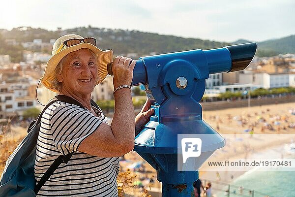 Seitenansicht einer glücklichen älteren Frau  die durch ein münzbetriebenes Fernglas schaut und lächelt