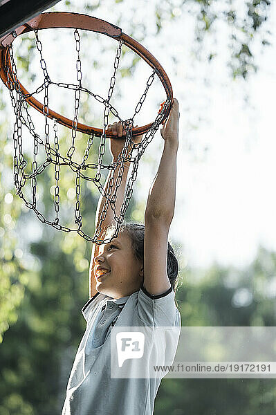 Smiling boy hanging on basketball hoop