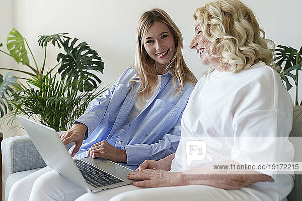 Smiling woman helping mother to use laptop