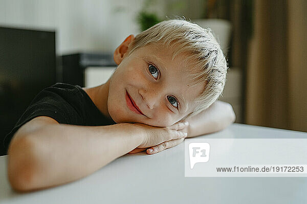 Smiling boy resting at table in home