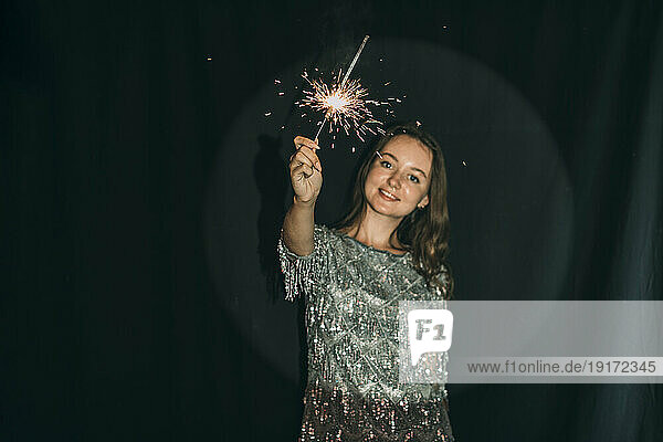Woman holding sparkler in front of black curtain