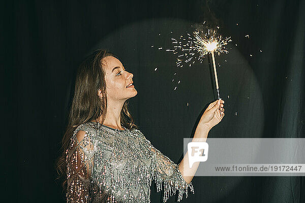 Smiling woman holding sparkler in front of black curtain