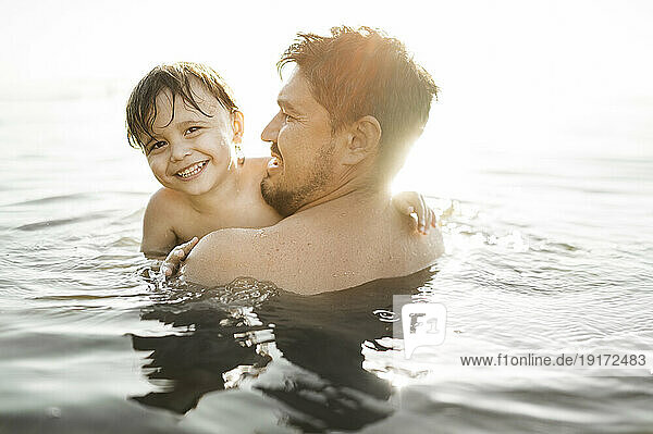 Happy father with son swimming in water on sunny day