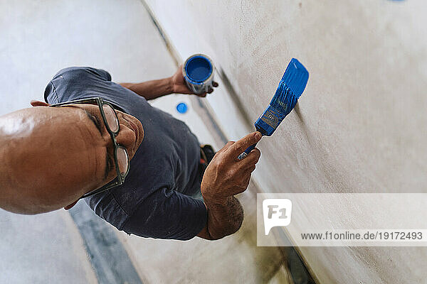 Bald construction worker applying blue paint on wall