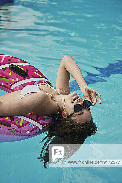 Teenage girl wearing sunglasses lying on swimming tube in pool