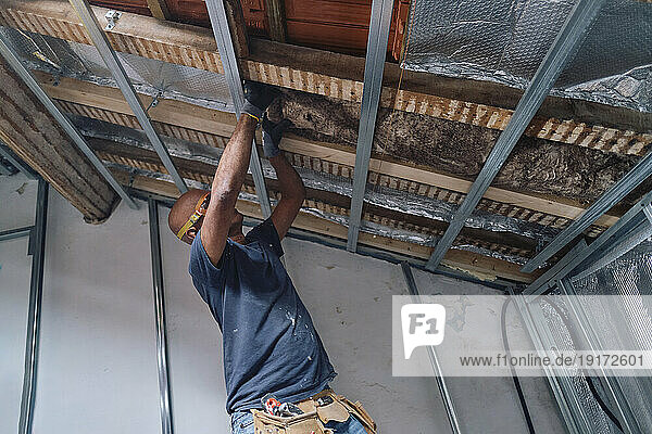 Construction worker installing insulation on ceiling in attic