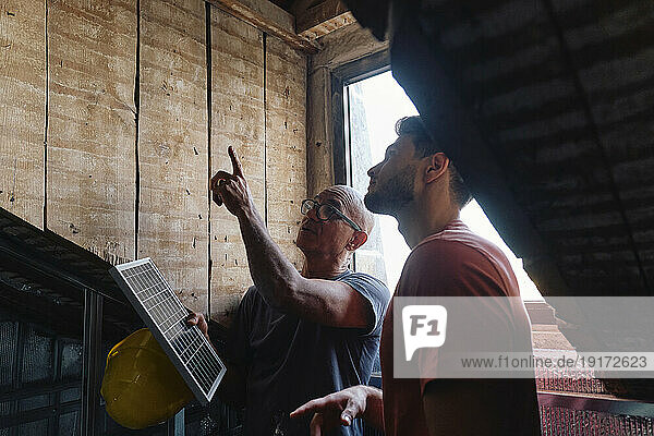Construction worker holding solar panel and discussing with man at site