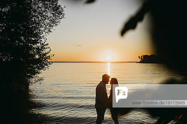 Man embracing woman in front of sea at sunset