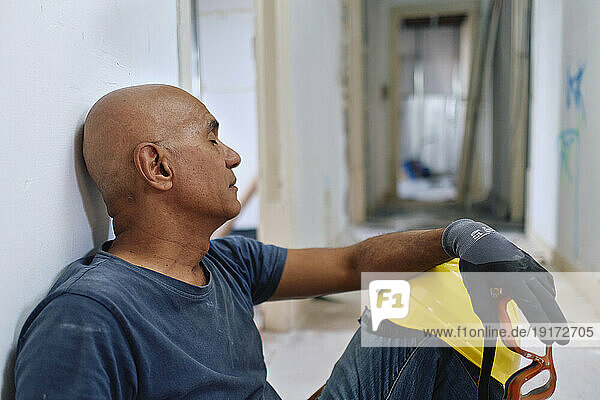 Tired construction worker sitting with eyes closed in corridor