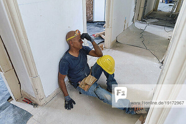 Tired construction worker touching forehead and sitting in corridor