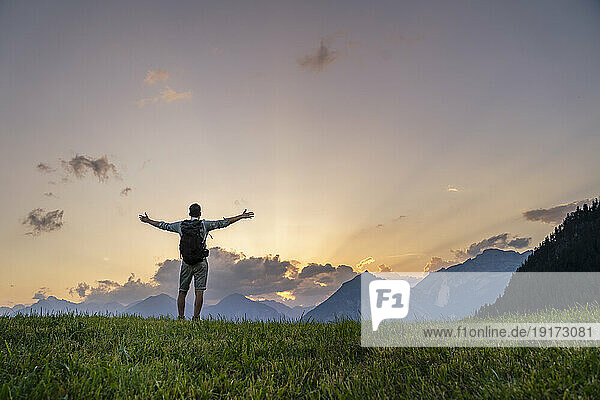 Man with arms outstretched in front of mountains at sunset
