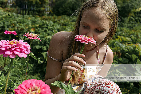 Blond girl smelling pink flower in garden