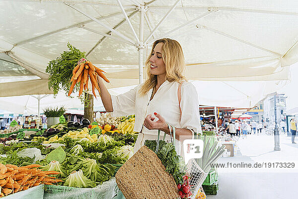 Happy woman buying bunch of carrots in market