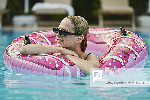Smiling teenage girl with inflatable swimming ring relaxing in pool