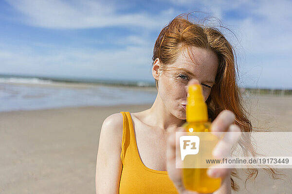 Redhead woman showing spray bottle at beach on vacation