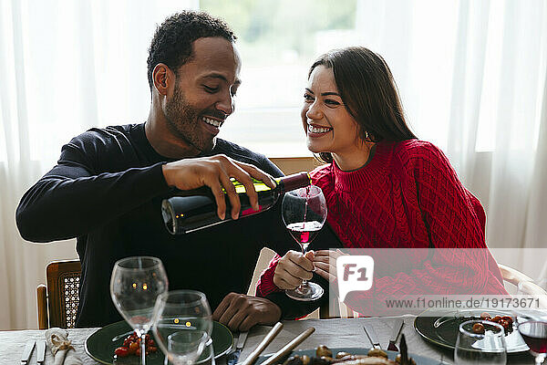 Smiling man pouring red wine to woman at dinner party