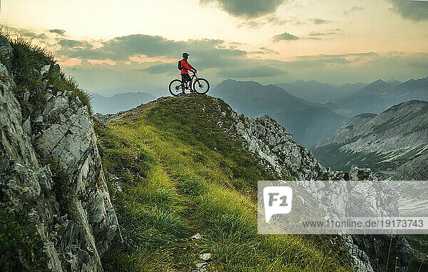 Active man with bicycle on mountain at sunset