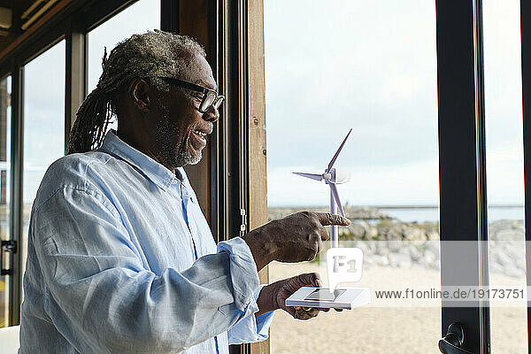 Happy engineer touching wind turbine model in cafe doorway