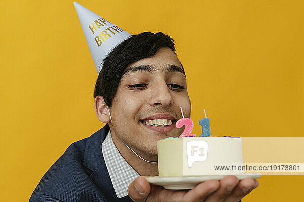 Happy man with party hat looking at 21st birthday cake