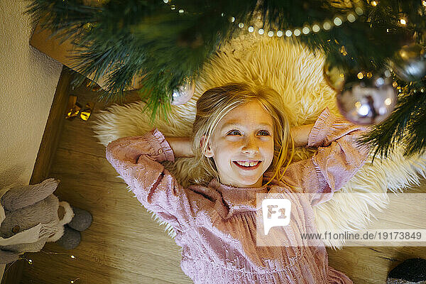 Smiling girl lying under Christmas tree at home