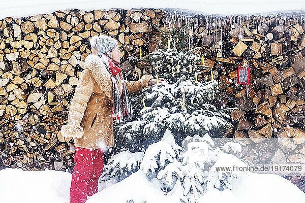Ältere Frau schmückt Weihnachtsbaum vor Feuerholz