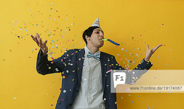 Young man blowing party horn and throwing confetti in studio