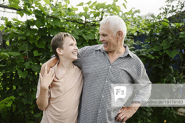 Happy grandfather standing with grandson in front of plants in garden