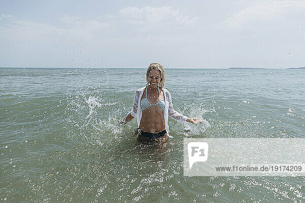 Smiling woman splashing water in sea