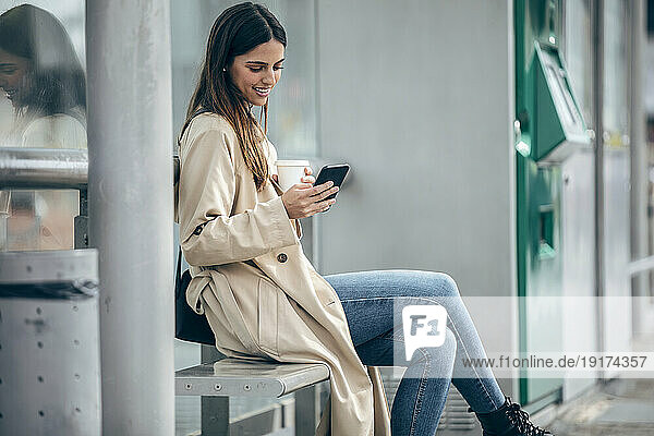 Happy woman sitting on bench and using smart phone