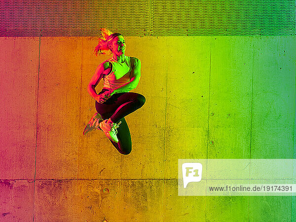 Active woman umping near neon colored wall