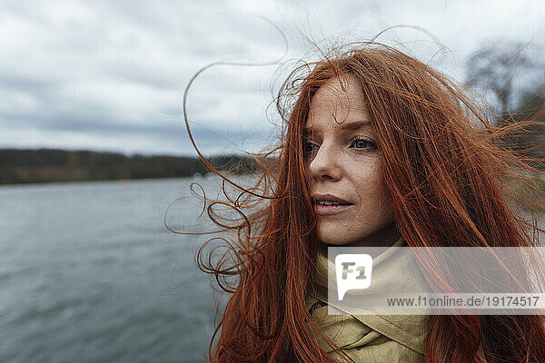 Thoughtful redhead woman in front of lake