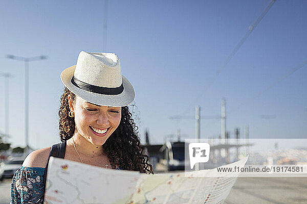Smiling woman wearing hat looking at map on sunny day