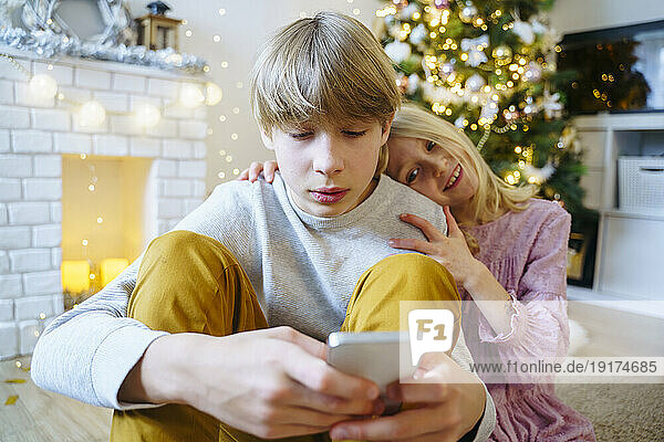 Boy using smart phone with sister at home on Christmas