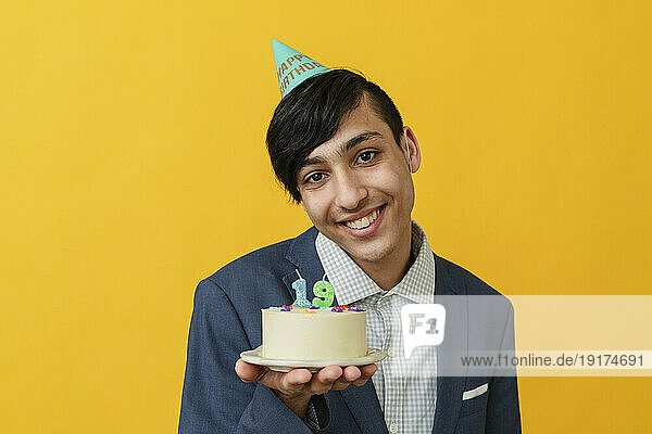 Smiling man showing birthday cake against yellow background