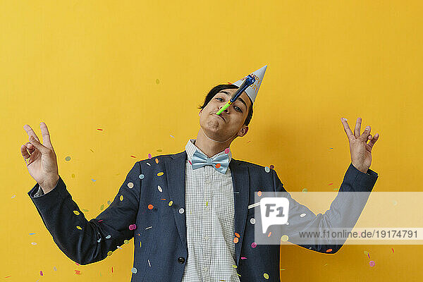 Young man gesturing peace sign and blowing party horn