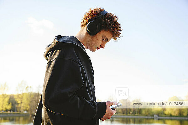 Teenage boy using mobile phone and listening music though headphones at park