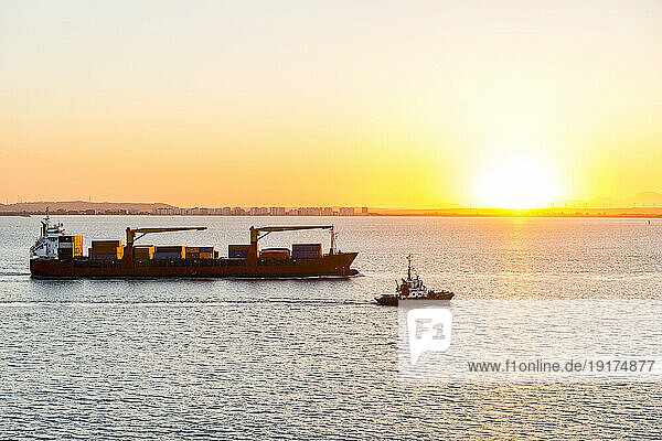 Spain  Andalusia  Cadiz  Boat sailing past moving container ship at sunset