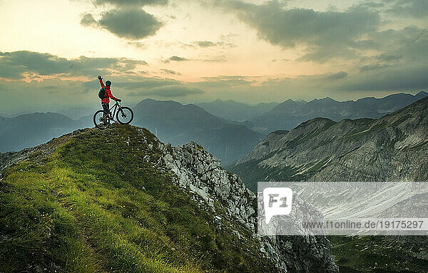 Active man with bike on mountain at sunset