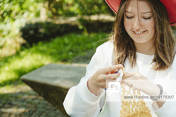 Smiling teenage girl knitting in park