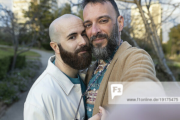 Smiling gay couple taking selfie in park at sunset
